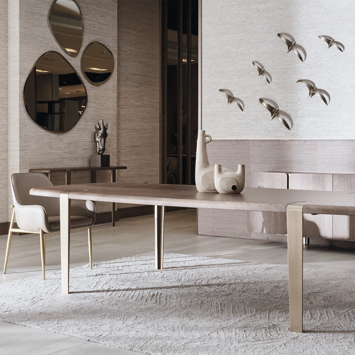 Oval marble dining table with sculptural wood base beneath a gold leaf wall sculpture